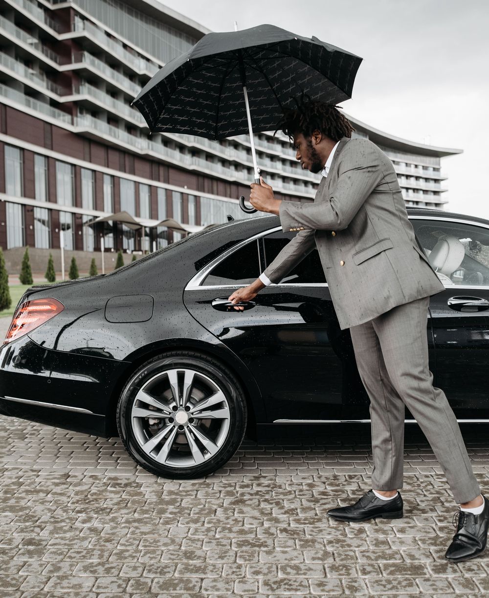 Chauffeur holding a rear door open beside a black sedan